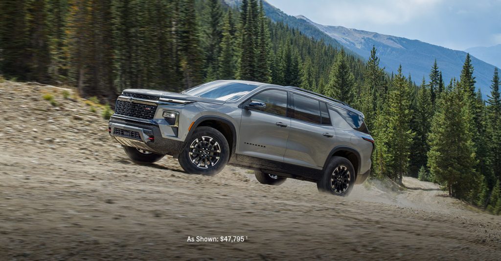 A silver 2025 Chevy Traverse driving uphill along a forested road near Turner Chevrolet.