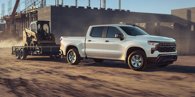 White Chevrolet Silverado towing equipment trailer at construction site