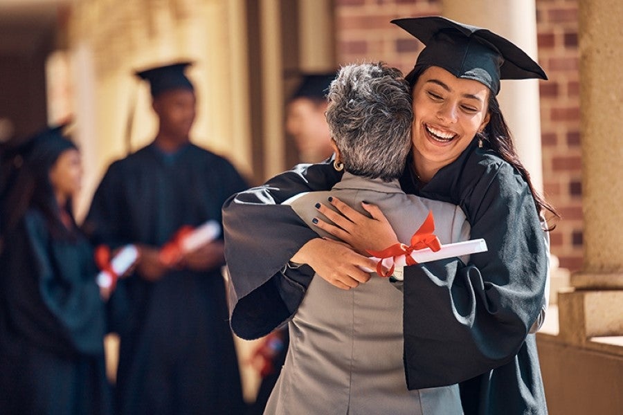 Graduate Lady having hug with another Lady surrounded by group of Student